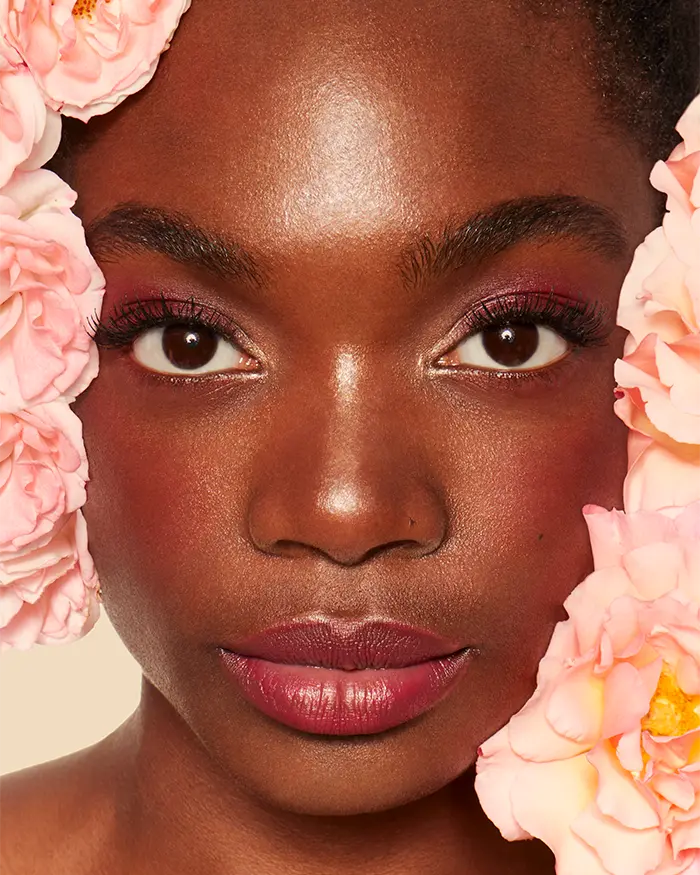 Nahaufnahme Beauty Bild einer Frau mit dunkler Hautfarbe blush und rosa Blumen die das Gesicht rahmen