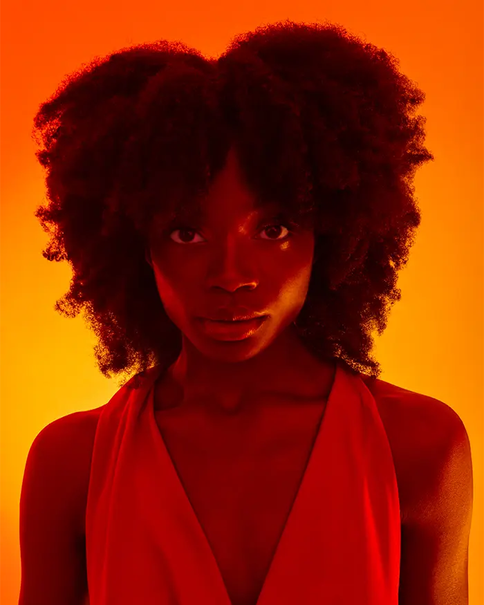 Schwarze Frau mit einem natürlichen Afrolocken in einem orangenen Sonnenuntergangslicht