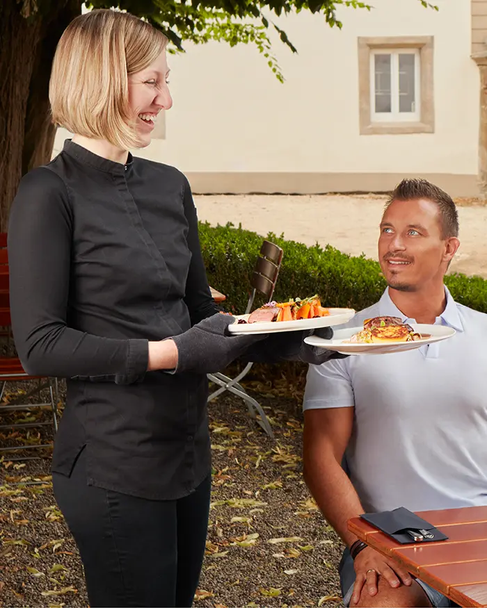 eine Bedienung die einem Mann das Essen an den Tisch bringt und freundlich lächelt