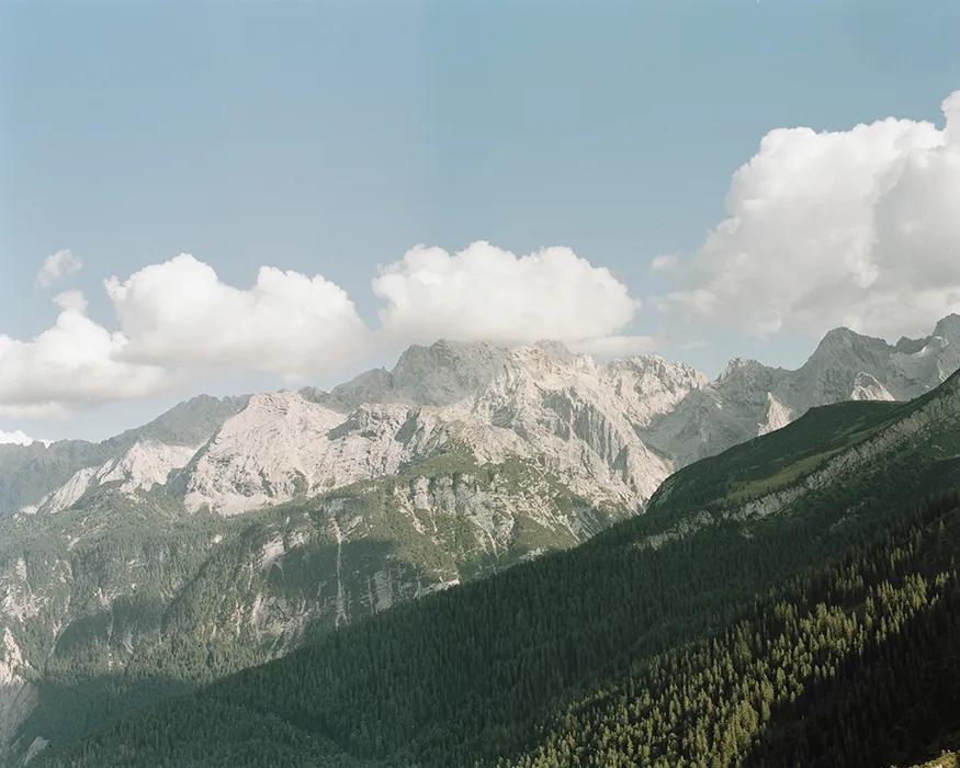 Berglandschaft in der Nähe der Zugspitze mit leichten Wolken vor strahlend blauem Himmel und grünen Wäldern
